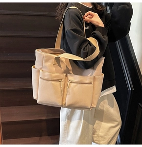 Close-up of beige canvas tote bag with front zipper pockets and wide shoulder strap