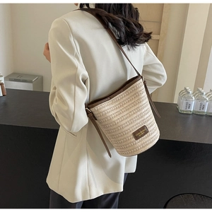 Close-up of beige woven bucket bag with brown leather trim and adjustable crossbody strap