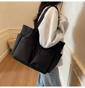 Detail of a large black canvas tote bag showing side thickness and durable strap on a model