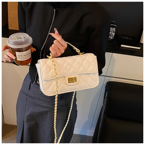 Detailed close-up of a white quilted patent leather handbag with gold chain strap