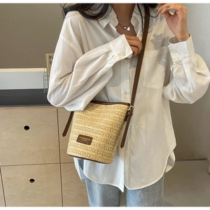 Detail of handwoven straw bucket bag with dark brown leather trim and thin strap