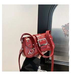 Macro detail of red patent leather shoulder bag featuring silver rivets and square buckle