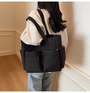 Detailed view of black canvas tote bag with functional zipper pockets and side compartments