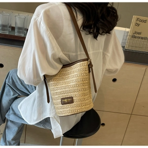 Detail shot of woven straw bucket bag featuring brown faux leather trim and brand patch