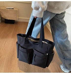 Detail of black canvas tote bag showing large capacity storage and two front zipper pockets