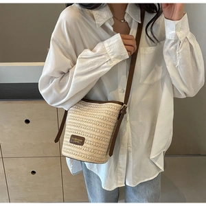 Detail view of woven straw bucket bag with dark brown leather straps and branding patch