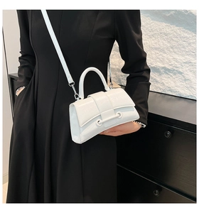 Close-up of a white patent leather handbag featuring curved flap and metal ring hardware