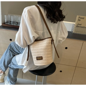 Detail view of woven straw bucket bag with dark brown leather trim and shoulder strap