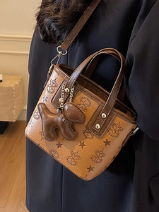 Sac seau monogramme marron avec breloque chien et bandoulière dans un décor de studio chaud
