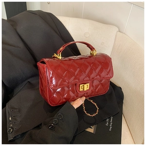 Detail of dark red patent leather handbag with quilted texture and gold lock