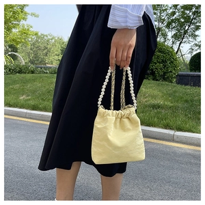 Details der hellgelben, plissierten Satin-Beuteltasche mit Perlengriff und Metallkette