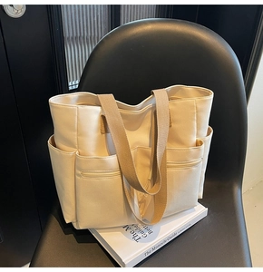 Detail of cream canvas tote bag featuring multiple front pockets and khaki webbing handles