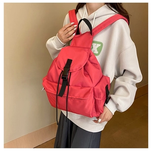 Detail of red nylon backpack showing flap buckle closure and front zipper pocket