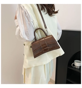 Detail of a dark brown glossy trapezoid handbag with retro texture and top handle