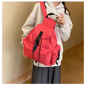 Detail view of the vibrant red nylon backpack with black buckle closure worn by a model