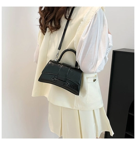 Close-up of black glossy patent leather hourglass handbag with curved base and metal ring