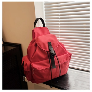 Detailed view of red nylon backpack with flap closure and black buckle on a windowsill