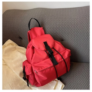 Detail of red nylon backpack with flap closure and adjustable buckles on sofa