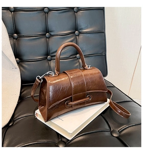 Close-up of a vintage brown glossy square handbag on white books over a black leather chair
