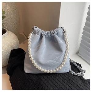 Hellblaue Beuteltasche mit weißem Perlengriff und Metallkette auf dunklem Stoff