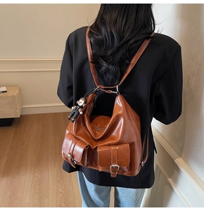 Detail view of brown faux leather backpack with double front buckle pockets and charm