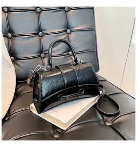 Detail of glossy pleated leather handbag with curved base and metal accent on a book