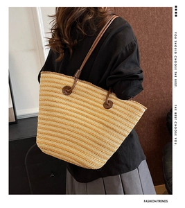 Détail d'un sac cabas tissé à rayures avec des anses en cuir marron porté par un modèle