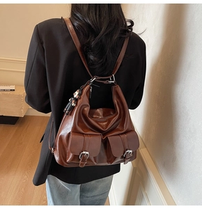 Detail view of a vintage dark brown leather backpack with two front pockets and bear charm