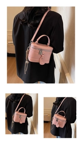 Detailed view of a pink box-style handbag with silver zippers and elegant side tassel accessory