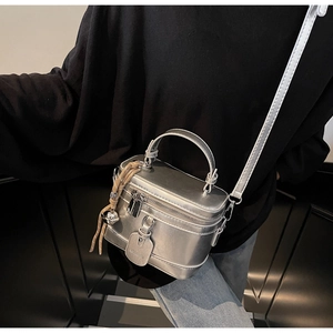 Detail of silver metallic box bag featuring a top handle, tassel charm, and thin strap