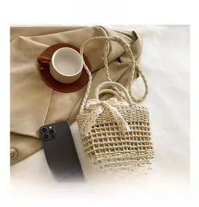 Detail showing handwoven cream beach bag size compared to a smartphone with lace bow decor