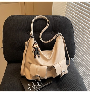 Detail of off-white faux leather tote bag with double buckled pockets and cute charm