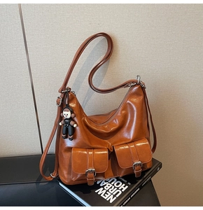 Detail of caramel oil-waxed leather tote bag with silver buckles on beige wall background