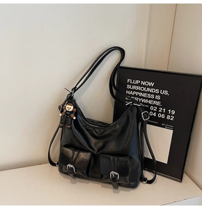 Close-up of black waxed leather tote bag featuring dual buckled front pockets and monkey charm