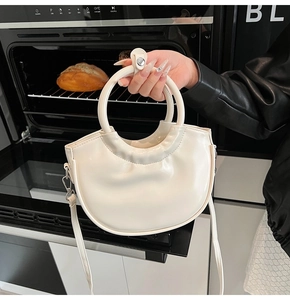 Close-up of cream semi-moon handbag with glossy PU leather and round hard handle