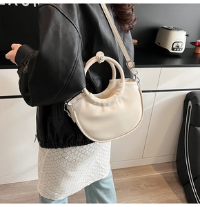 Model wearing a cream white crescent handbag with a round handle and silver hardware