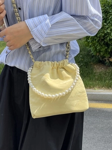 Minimalistische hellgelbe Beuteltasche mit Perlengriff und Kettenriemen am Modell