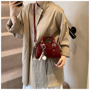 Detail of glossy deep red Boston bag with silver buckle and unique baseball pendant charm