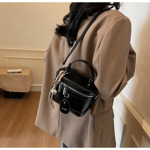 Detail view of a black glossy mini box bag with twin zippers and a decorative charm pendant