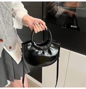 Detail of glossy black leather handbag with a circular top handle and slender shoulder strap