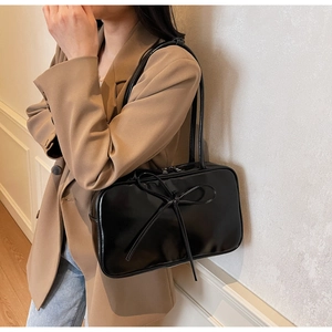Detail view of black glossy Boston shoulder bag with delicate bow knot on beige suit