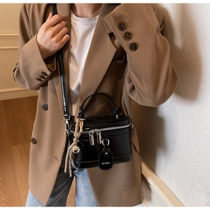 Detail of a black patent leather box bag with a top handle and adjustable shoulder strap