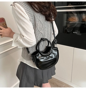 Detail of black glossy leather crescent bag with metallic round handle and slim shoulder strap