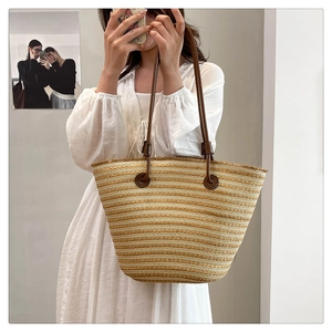 Détail d'un cabas en paille tressée avec anses en cuir marron porté avec une robe d'été