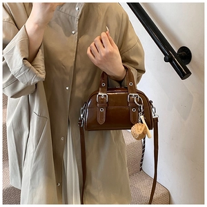 Detail of a dark brown glossy Boston bag with silver buckles and a strawberry charm detail