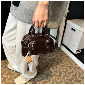 Detail of dark brown patent leather boston bag with silver buckles and baseball charm