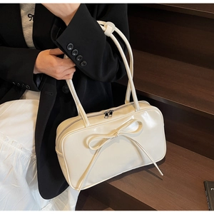Close-up of a white Boston bag featuring a large bow decoration and smooth leather texture