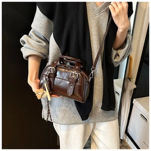 Detail of dark brown glossy Boston bag featuring silver hardware and a baseball pendant charm