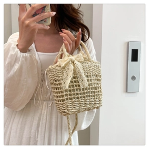 Detail of light beige straw handbag featuring a large lace bow and drawstring inner pocket