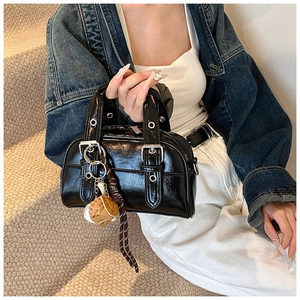 Close-up of black glossy Boston bag with silver metal eyelets and a baseball charm